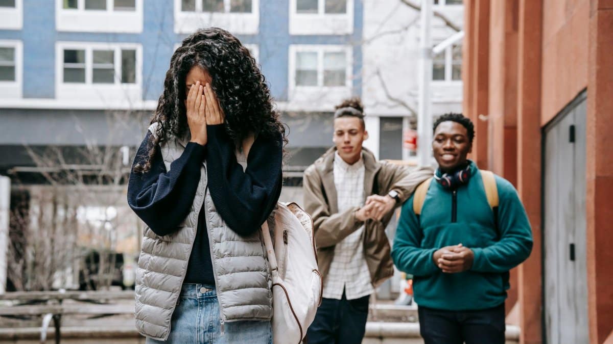 Unrecognizable young female student covering face with hands while being bullied by multiethnic male classmates on street