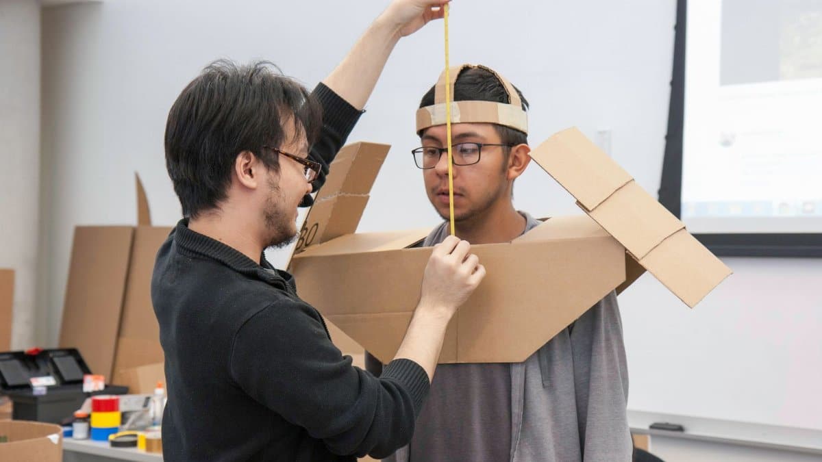 Two students collaborating on creating a cardboard costume during a classroom project activity.
