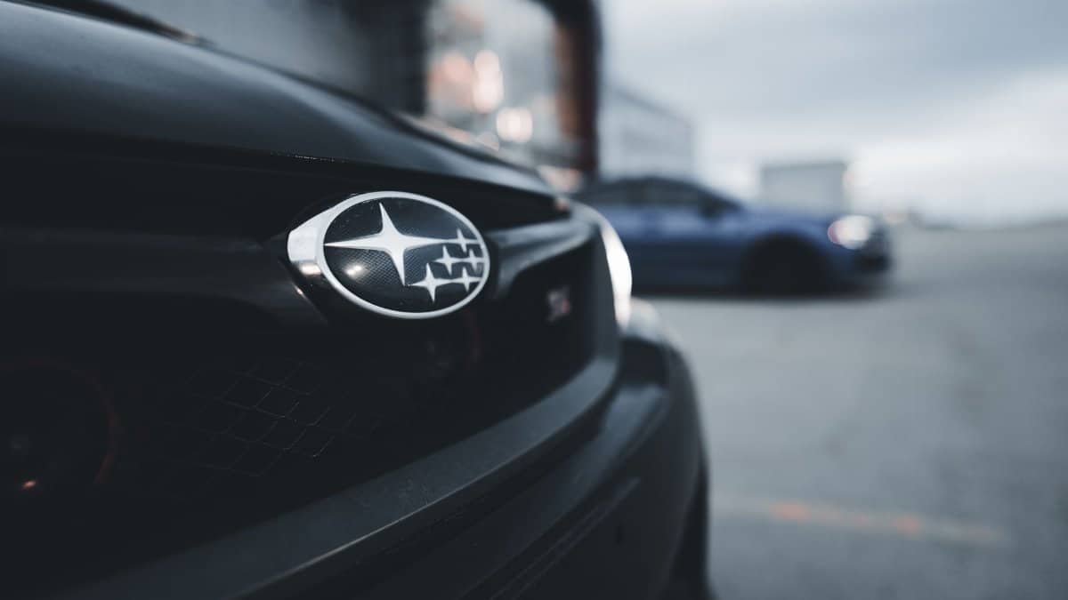 Detail of a Subaru WRX grille with an out-of-focus background featuring another car.