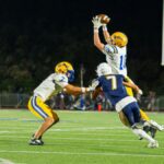 High school football players in a dramatic mid-air catch during a night game.