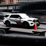 A sheriff vehicle parked on a busy urban street with motion blur of passing cars and vibrant orange cones.