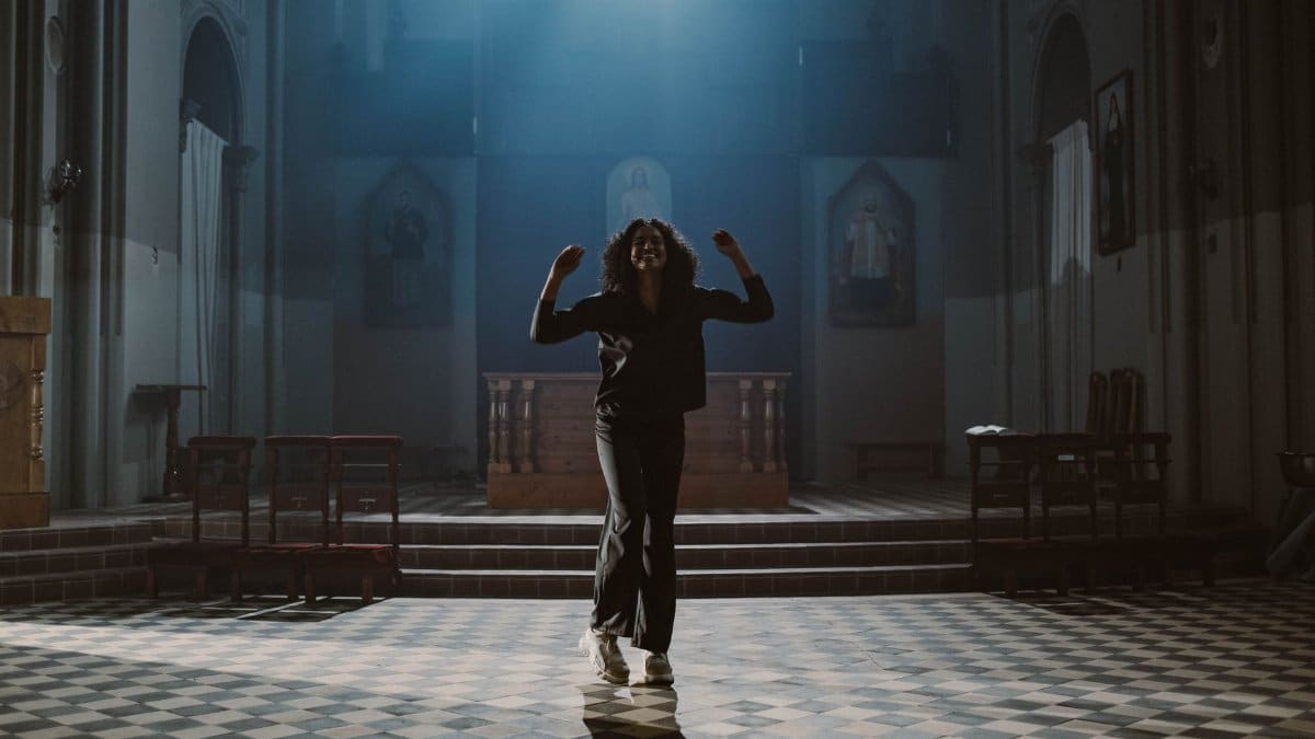 A woman dances joyfully in a beautifully lit church interior, bathed in sunlight and shadow.