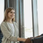 Woman smiling and shaking hands at a business office, signaling a successful job interview.