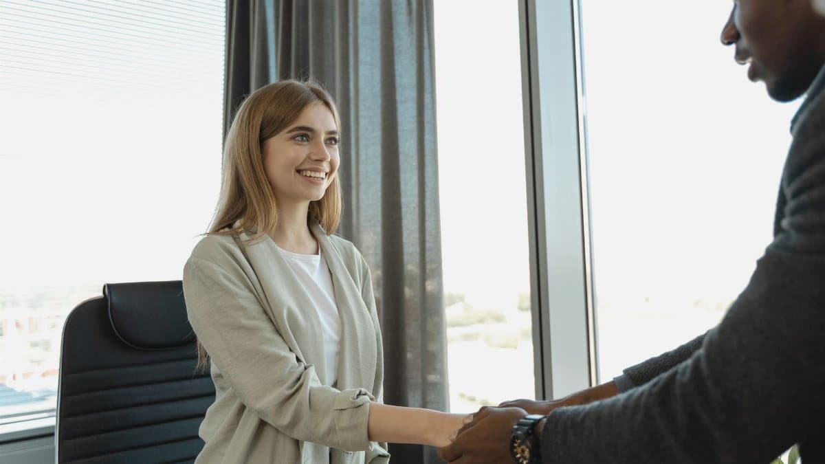 Woman smiling and shaking hands at a business office, signaling a successful job interview.