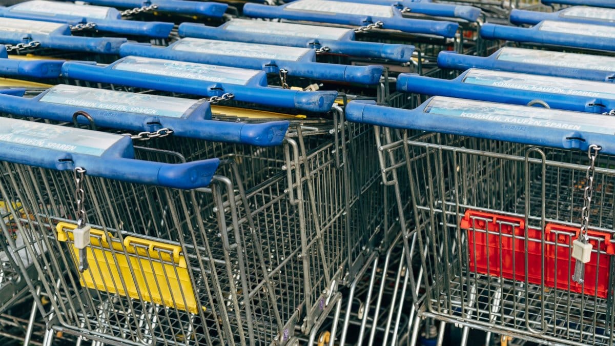 Metallic row of shopping carts with blue handles in a supermarket setting.