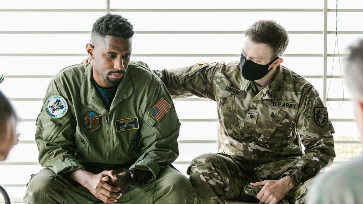 Two military personnel engaged in an emotional support session indoors.