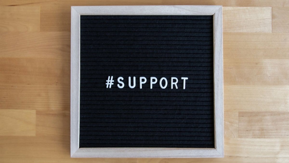Black letter board displaying the word '#support' on a wooden table surface.