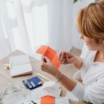 A woman organizing her finances with bills and receipts at a home office desk using a calculator and laptop.