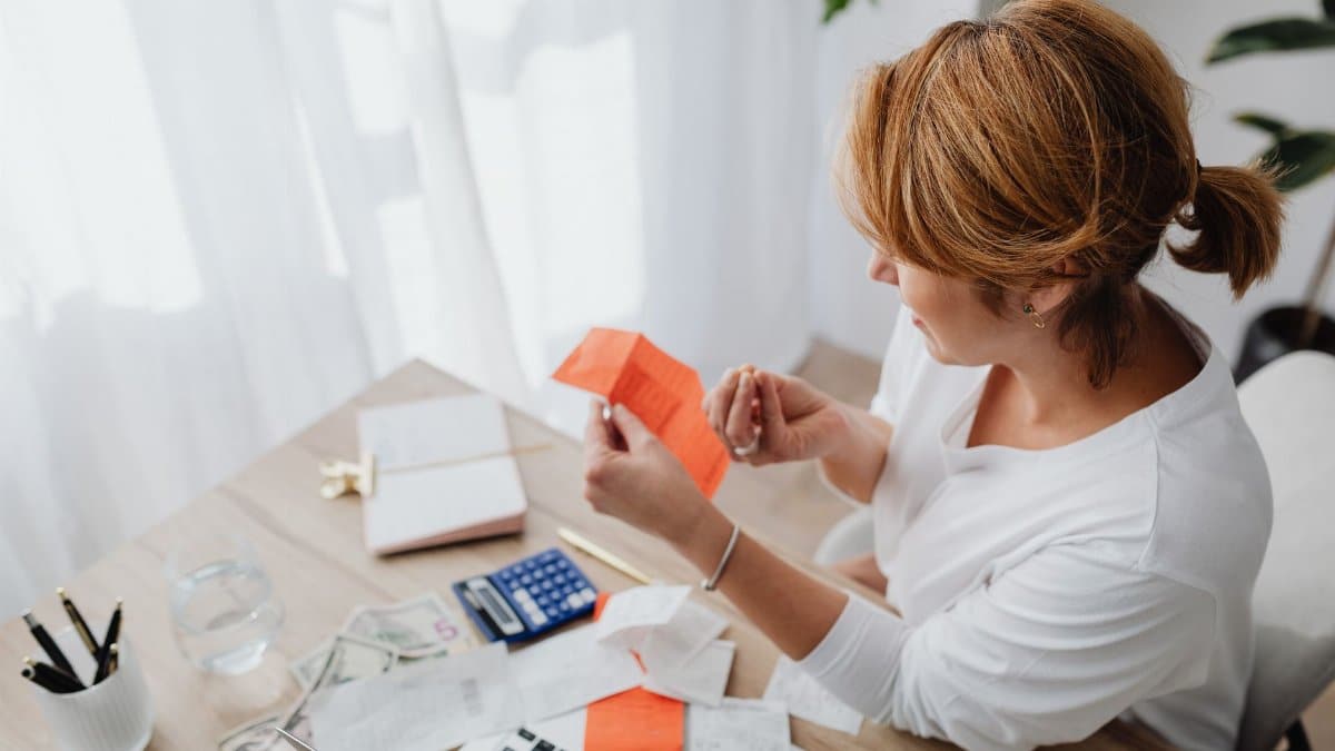 A woman organizing her finances with bills and receipts at a home office desk using a calculator and laptop.