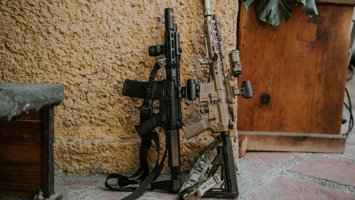 Two tactical rifles leaning against a rustic wall, showcasing military equipment.