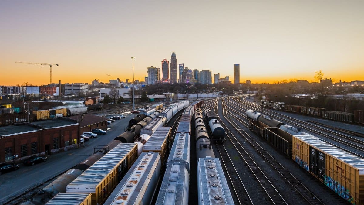 Dramatic sunset over Charlotte's skyline with cargo trains heading into the city, showcasing transportation and urban life.