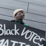 Low-angle shot of an activist holding a Black Votes Matter placard during a protest.