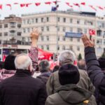 Crowd at a public rally with flags raised, focusing on community spirit and engagement.