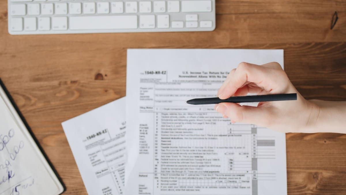 Close-up of a hand holding a pen over US tax forms on a wooden table.