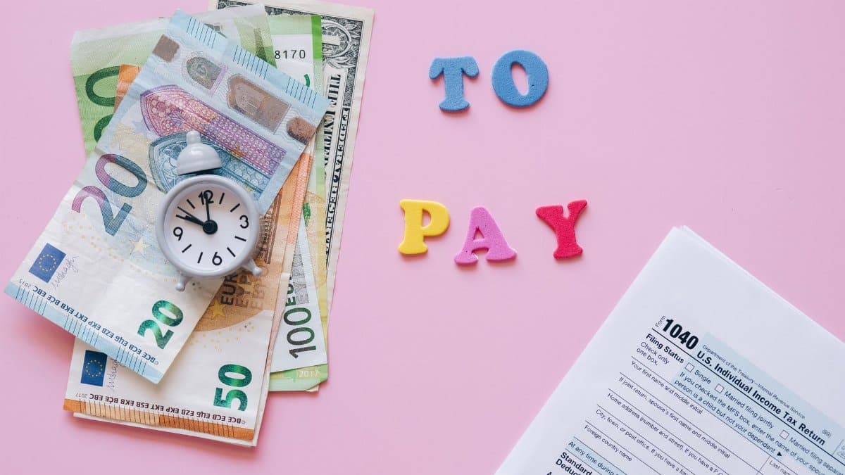 Flat lay of taxes, currency, and reminder to pay on pink background.