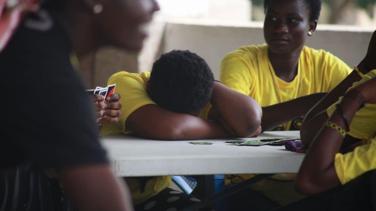 Group of teenagers in yellow shirts play cards at a table, enjoying leisure time.