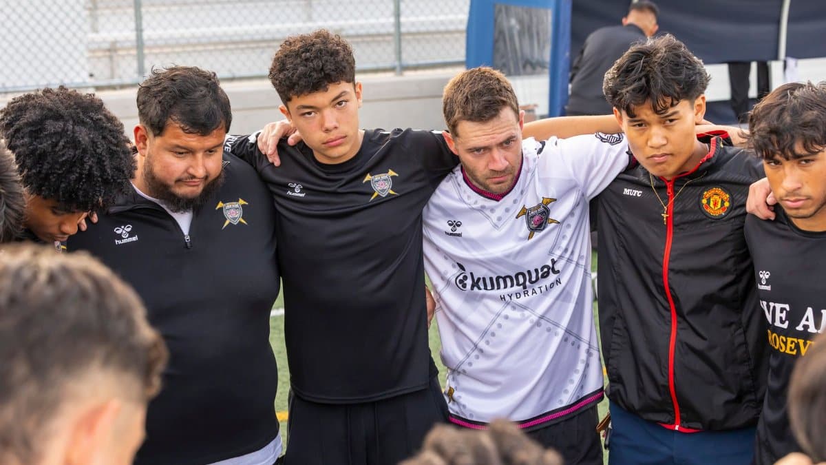 A soccer team group huddle shows unity and teamwork on an outdoor field.