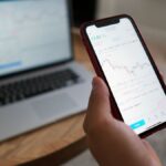 A person trading stocks on a smartphone and laptop. Ideal for finance themes.