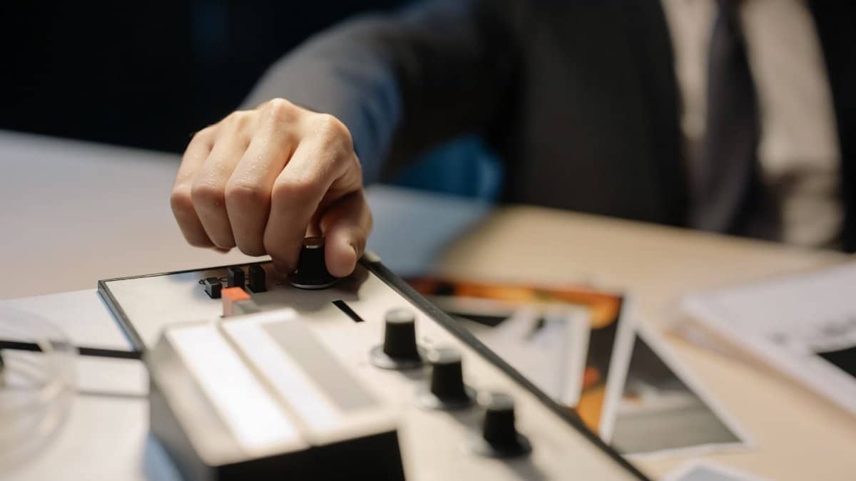 A detective's hand adjusts knobs on a vintage tape recorder, suggesting investigation or espionage.