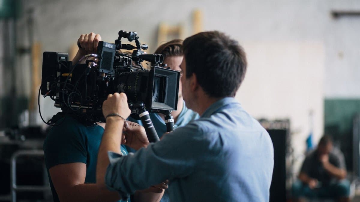 A film crew adjusting a video camera on an indoor set, focusing on technical preparation and teamwork.