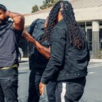 Two law enforcement officers detain a man during a daytime arrest outside a building.
