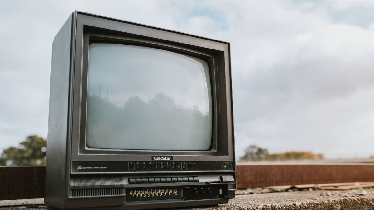Black old fashioned obsolete television with reflection on screen placed on concrete railing against cloudy ski on street on blurred background