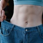 A woman shows her weight loss by holding oversized jeans revealing her toned stomach.