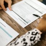 Close-up of two people reviewing and filling out a credit card application on a wooden table.