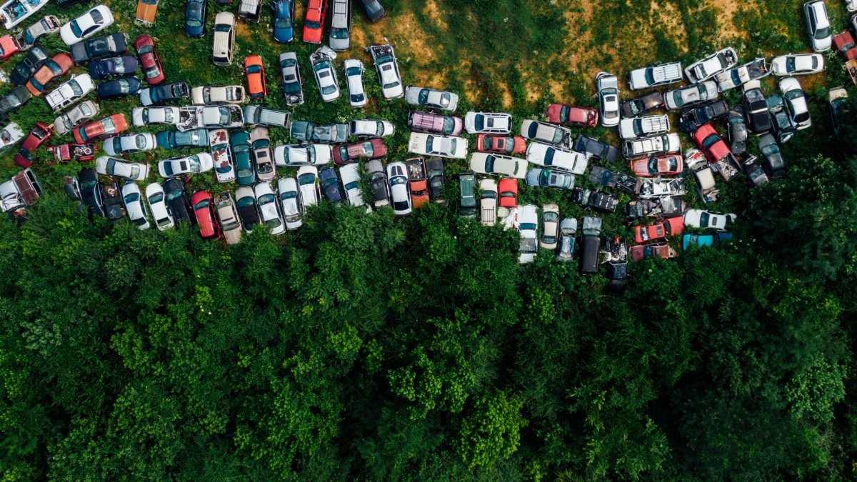 Aerial shot of a junkyard with abandoned cars surrounded by greenery.