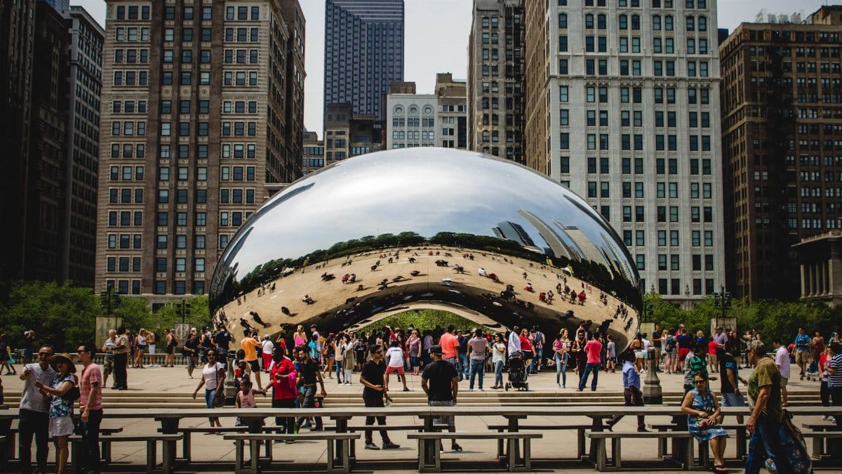 People gathering around Cloud Gate in Chicago with reflections of cityscapes. Popular tourist spot in Millennium Park.
