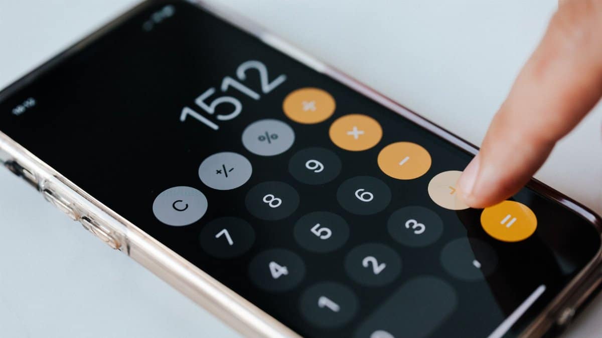 From above of crop faceless financier touching plus sign on screen of cellphone while using calculator application and calculating total amount