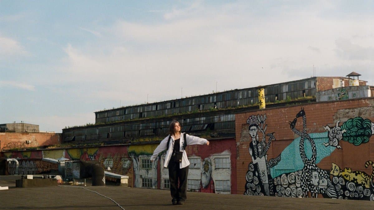 Woman walking on a rooftop with colorful street art mural in urban setting.