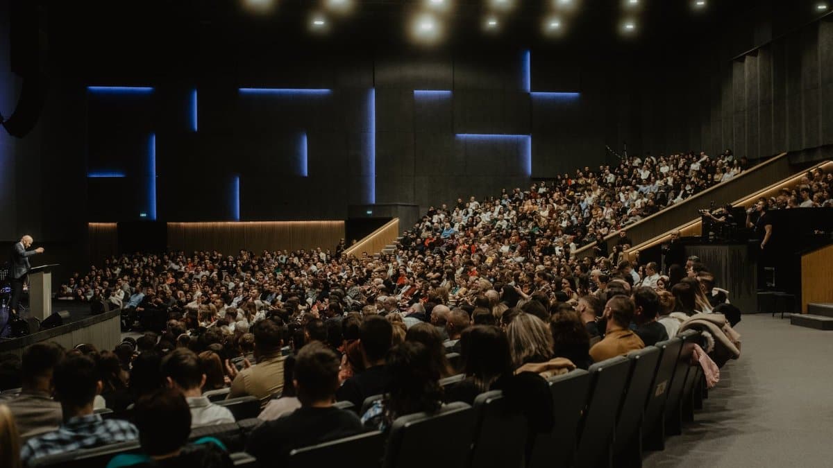 A large audience attentively listens to a speaker at a conference in Oradea, Romania.
