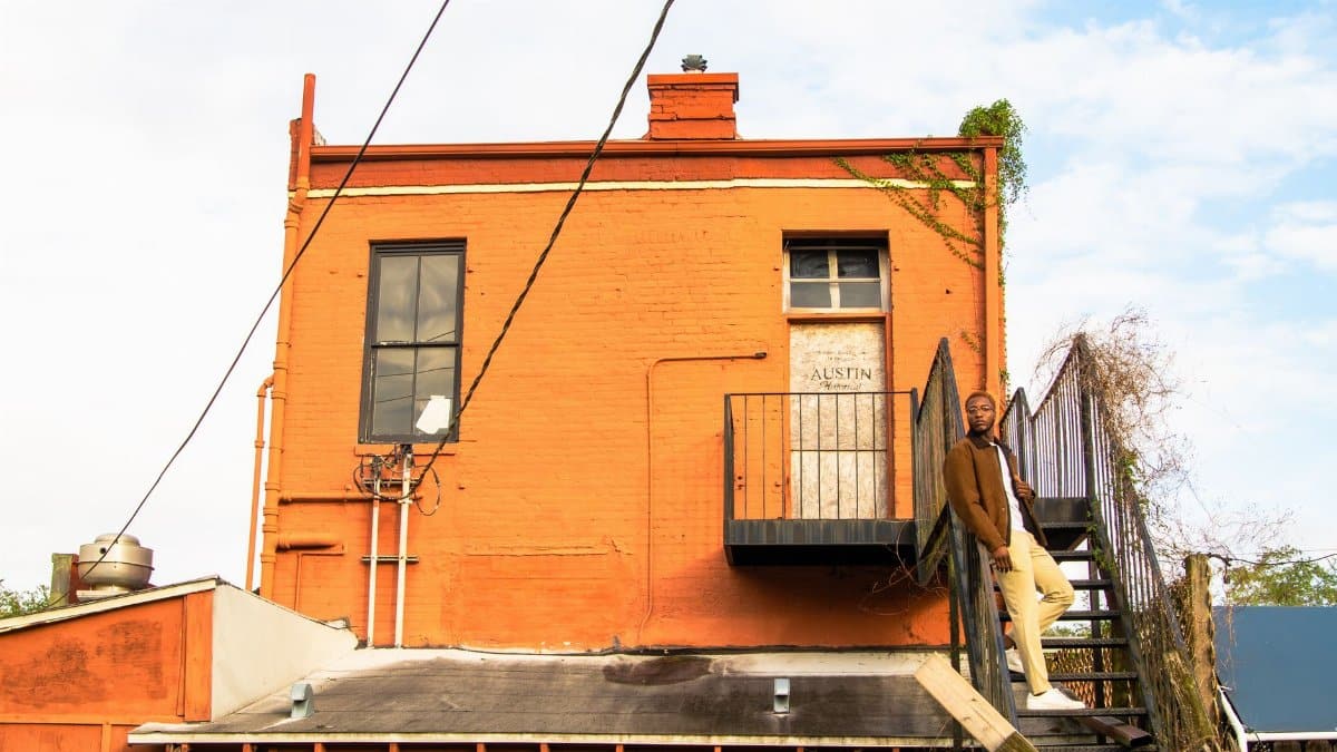 Stylish man standing on stairs of a vibrant orange building in Austin, Texas.