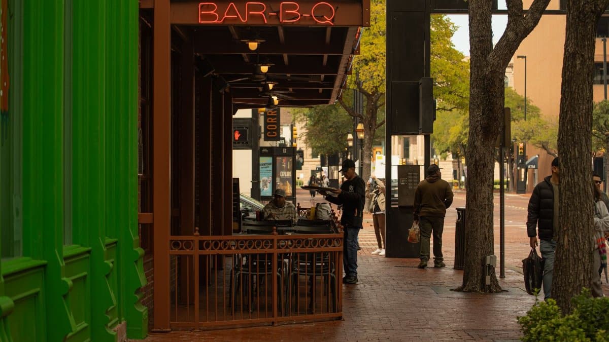 Downtown street with BAR-B-Q sign and people enjoying a city vibe.