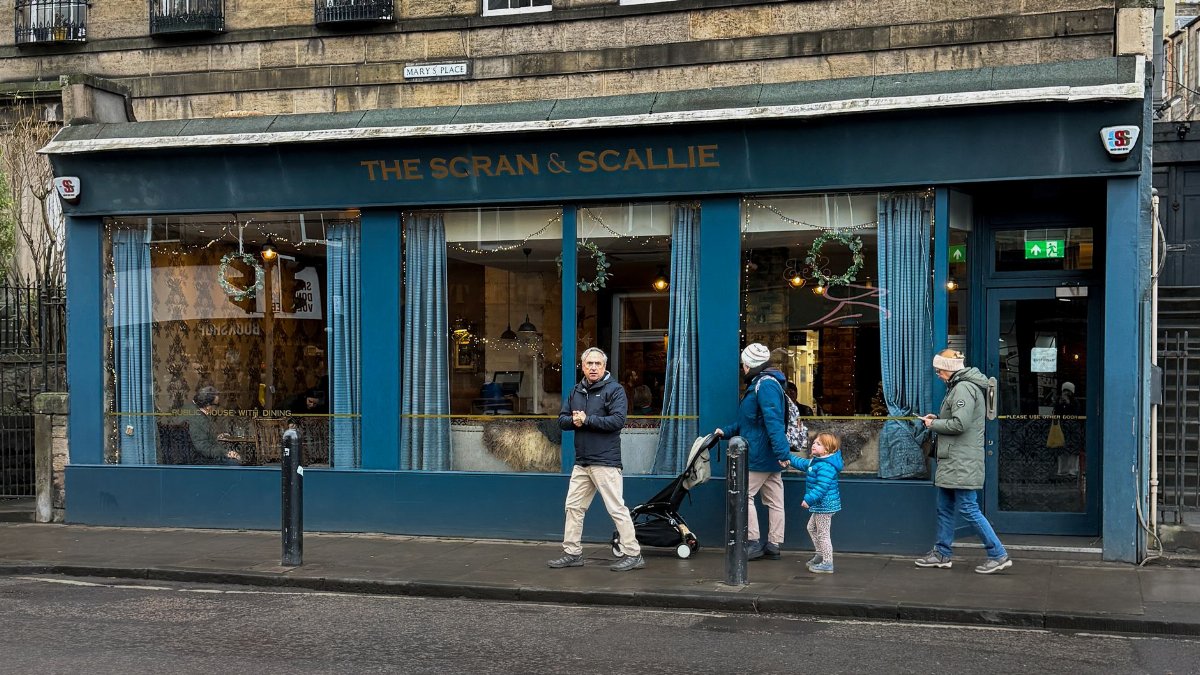 People walking outside The Scran & Scallie restaurant in Edinburgh's charming cityscape.