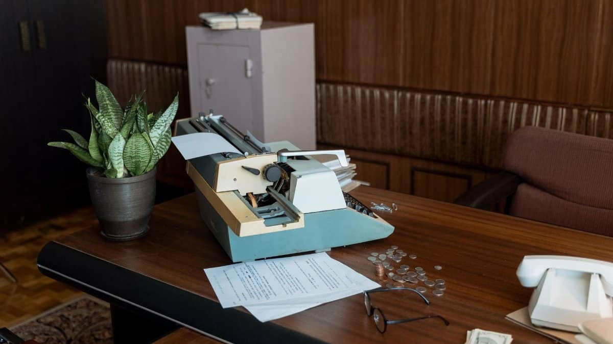 Retro office setting with a vintage typewriter, papers, and coins on a wooden desk.