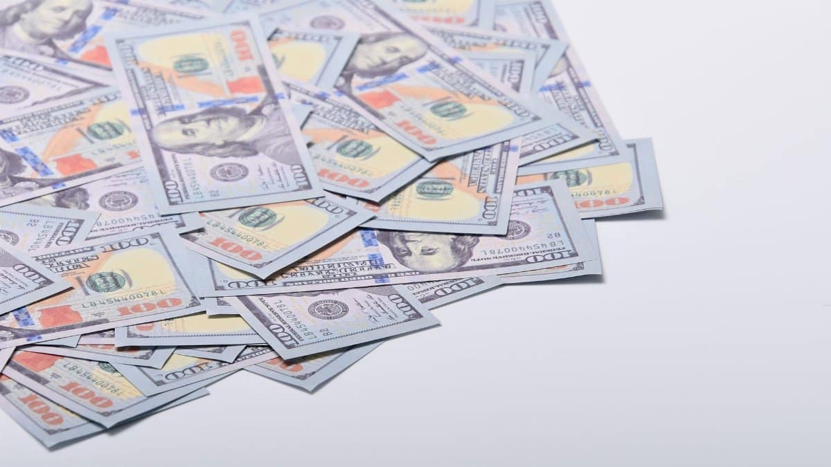 A scattered pile of US hundred dollar bills on a clean white surface.