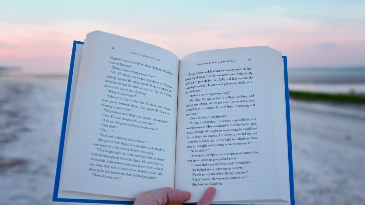 A hand holding an open book against the scenic backdrop of a beach at sunset on Hilton Head Island.