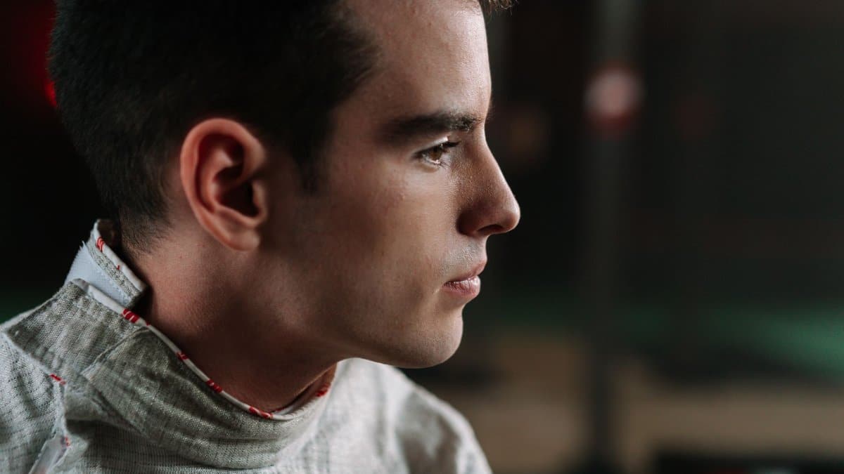 Close-up profile of a male fencer concentrating ahead, wearing fencing uniform.