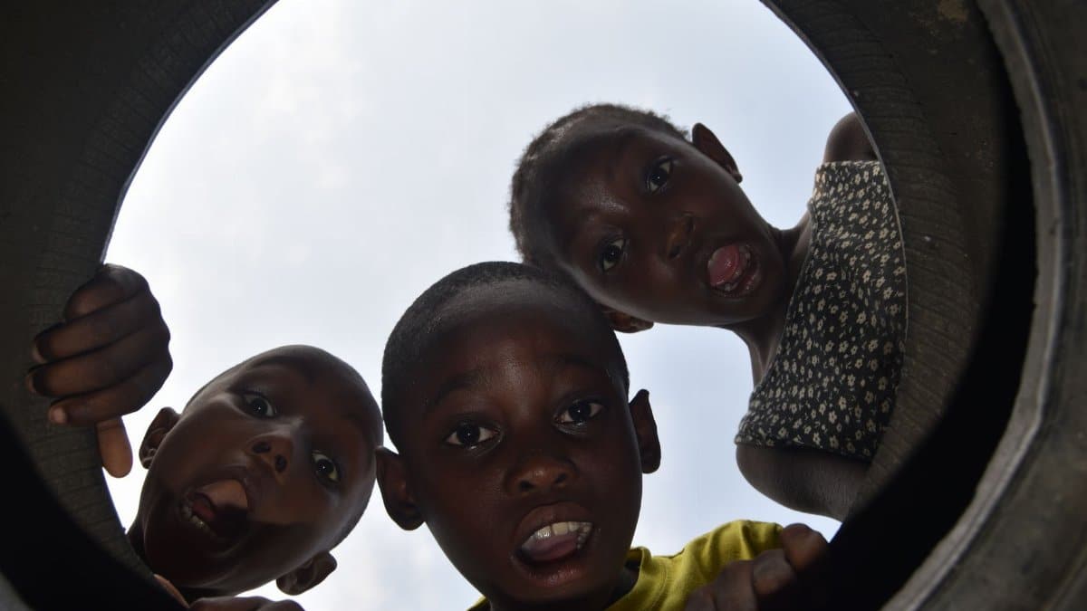 Three curious children in the Republic of Congo peer through a circular opening with expressive faces.