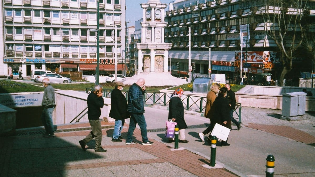 City street view with people walking near a prominent clock tower on a sunny day.