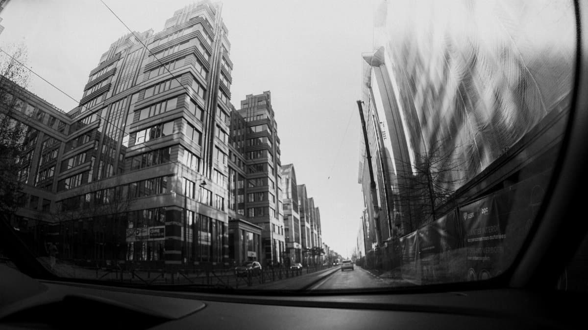 Black and white view of modern city buildings from inside a car.