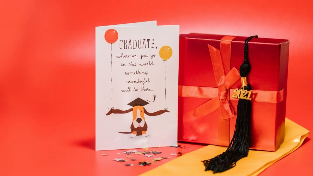 Celebrate graduation with a festive card, gift box, and tassel on a vibrant red backdrop.