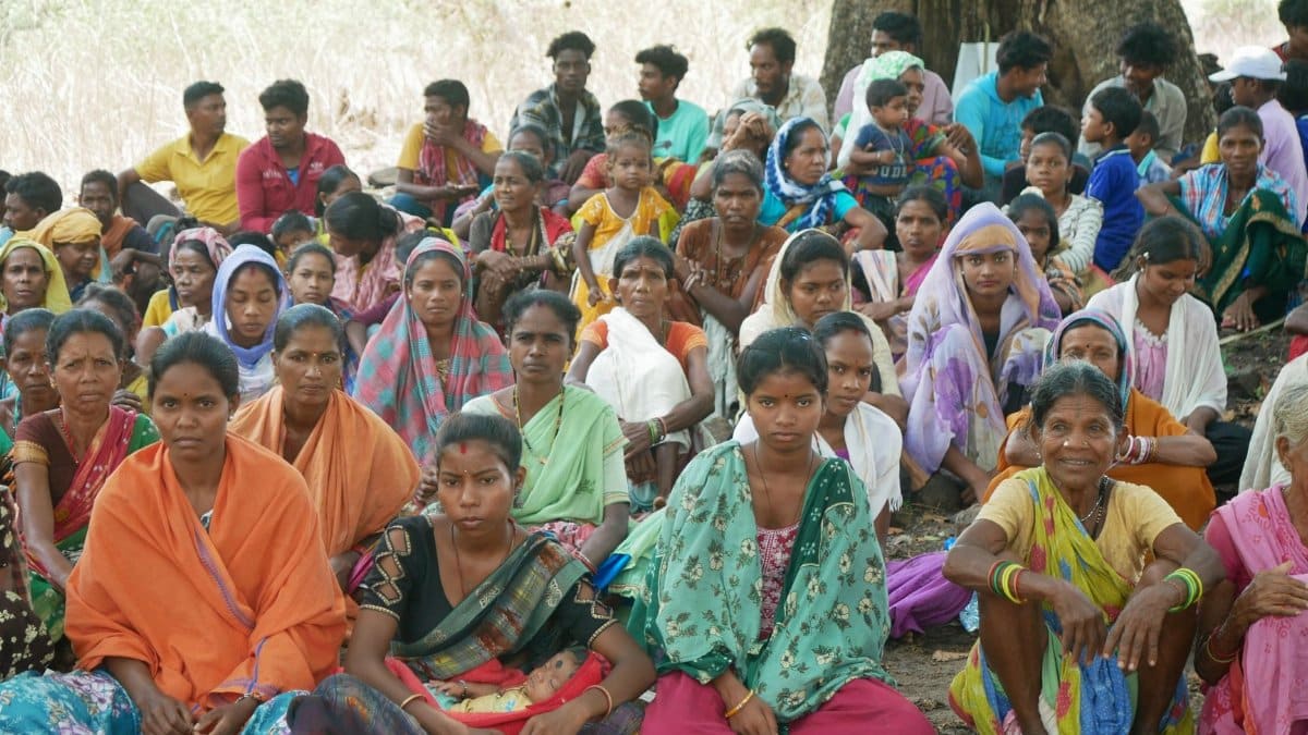 A large group of people sitting outdoors under a tree, showcasing diversity and unity.