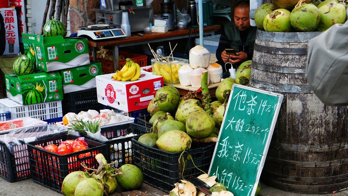 A bustling outdoor market stall featuring fresh coconuts, watermelons, and bananas.