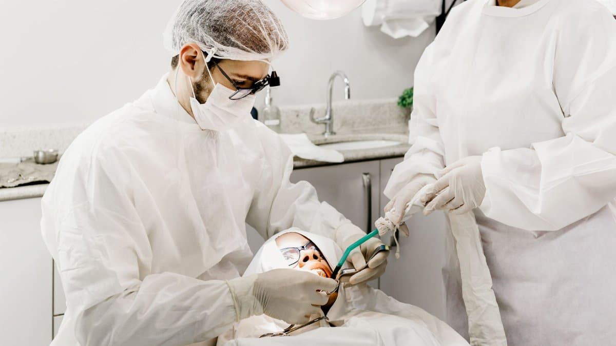 From above of unrecognizable male stomatologist and female assistant in uniforms treating patient teeth in clinic