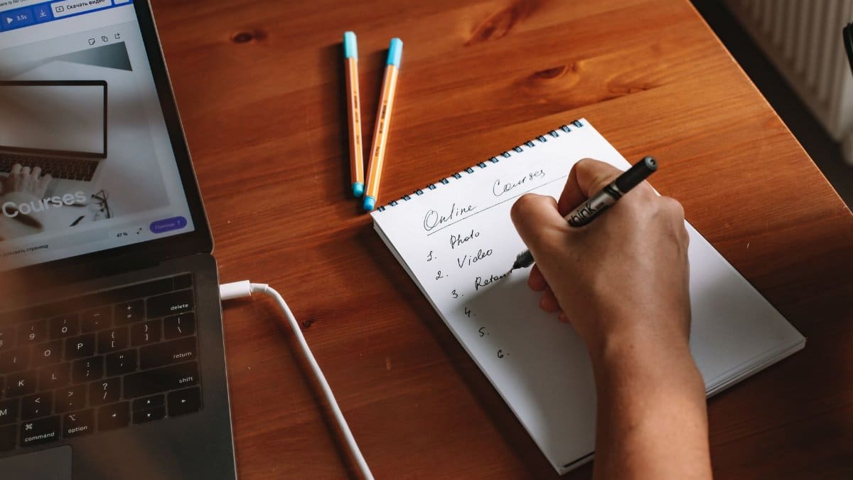 Photo of a person writing a list of online courses on a notepad next to a laptop.