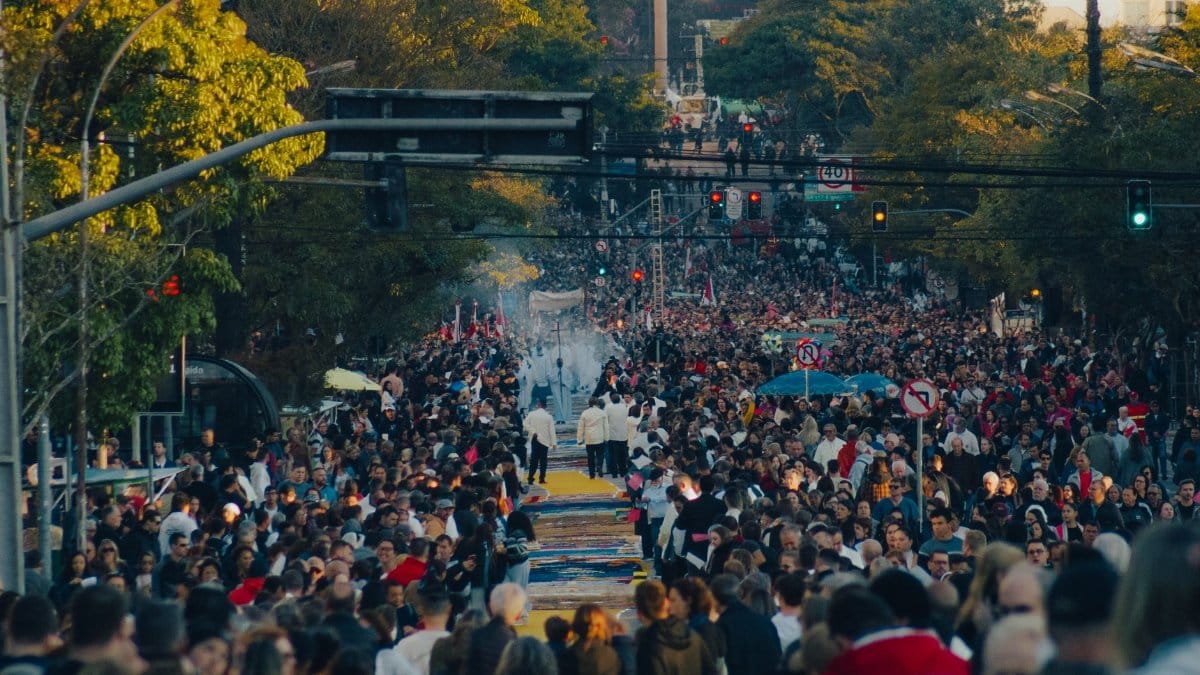A large crowd gathers for an urban street procession under a clear sky.