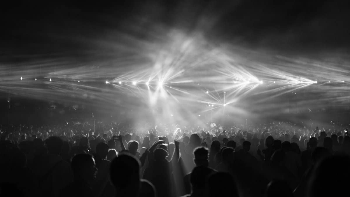 A dramatic black and white photo capturing a crowd at a night concert with bright stage lights.